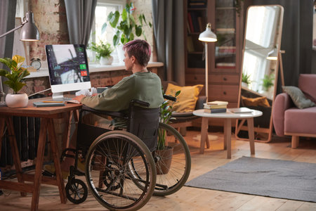 Rear view of disabled woman working as a programmer on computer with new software in domestic roomの写真素材