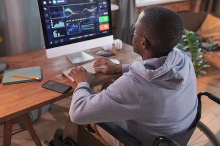 Rear view of African disabled man typing on computer developing new software while working at homeの写真素材