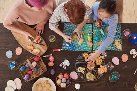 High angle view of happy children and young mother decorating cookies in the kitchen preparing for...