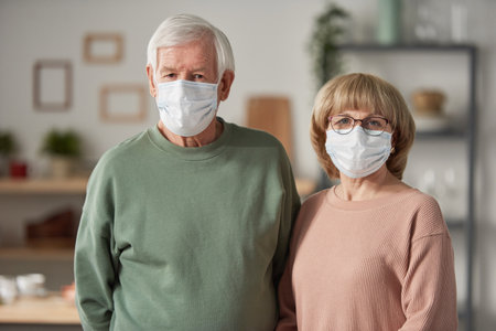 Portrait of senior couple in protective masks looking at camera standing in the roomの写真素材