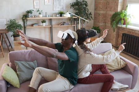 Playing video game in team sitting on sofa at home