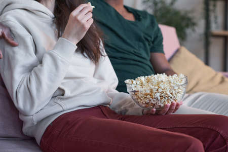 Couple eating popcorn sitting on sofa at home