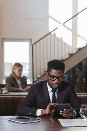 African young businessman using digital tablet while working online sitting in coffee shopの写真素材