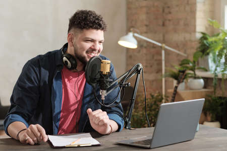 Happy young male radio host broadcasting through microphone in studioの写真素材