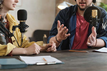 Close-up of young people sitting at the table with microphones and discussing with each other during broadcastingの写真素材