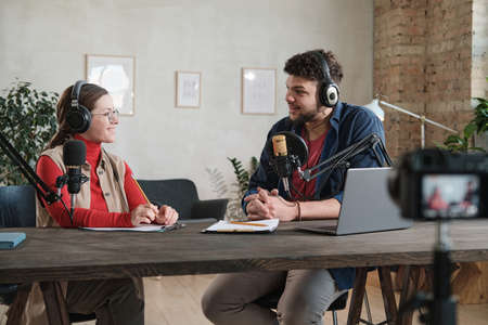 Young man in headphones interviewing a woman at the table during broadcasting at radio studioの写真素材