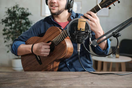 Close-up of musician sitting in front of microphone and playing guitar in recording studio