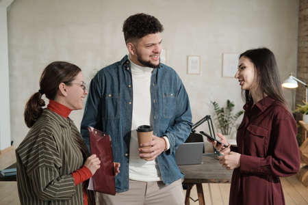 Group of young business people talking to each other while standing at officeの写真素材