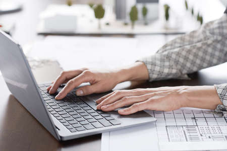 Close-up of businesswoman sitting at her workplace and working online typing on laptop computer