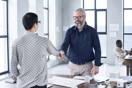 Business partners standing and shaking hands to each other over the table to conclude a contract at officeの写真素材