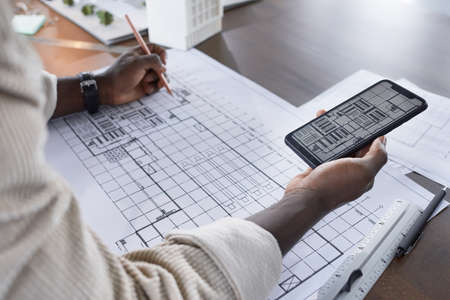 Close-up of architect using the photo on his mobile phone and drawing the copy on the paper at the tableの写真素材