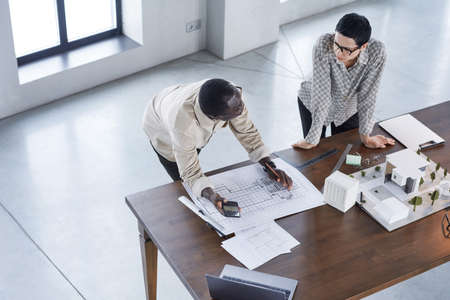 High angle view of two engineers developing new project together they working over blueprints and model of buildingの写真素材