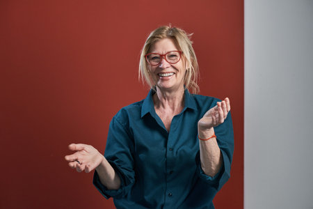 Portrait of happy senior woman in blue blouse standing and laughing against the red backgroundの写真素材