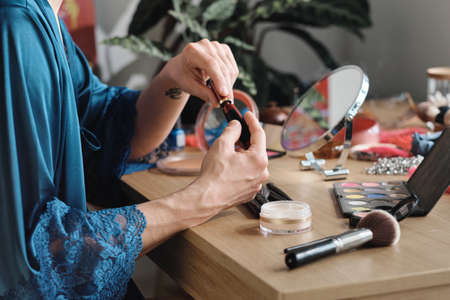 Close-up of man sitting at the table and using lipstick in makeup during preparation for performance
