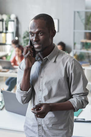 African young businessman discussing work with his partner using mobile phone while standing at officeの写真素材