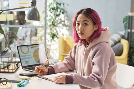 Portrait of Chinese student looking at camera while studying at her table with laptop