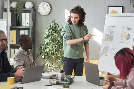 Young businessman pointing at flip chart and presenting his project to the colleagues during...