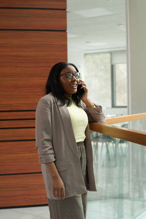 African smiling businesswoman having a conversation on mobile phone while standing at office
