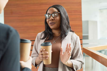 African young businesswoman drinking coffee and talking to her colleague during coffee breakの写真素材