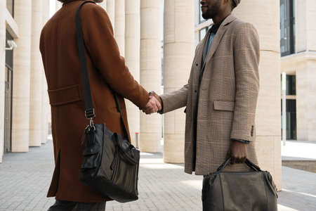 Two young businessmen shaking hands during their meeting in the city