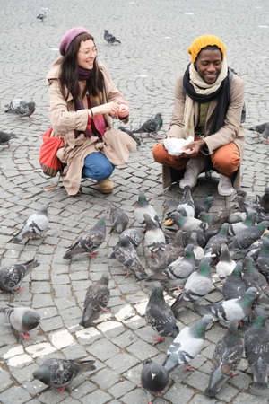 Young couple feeding birds together during their walk in the cityの写真素材