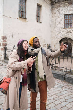 Happy young couple of tourists going sightseeing and making photos on the phone in the cityの写真素材