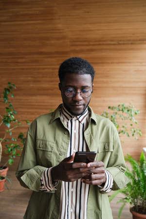 African young businessman typing a message on mobile phone while standing at officeの写真素材