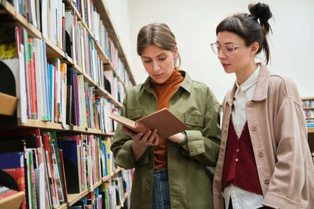 Two young women choosing books for study while standing in the libraryの写真素材