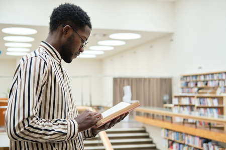 African young man in eyeglasses learning in the library he standing and reading a bookの写真素材
