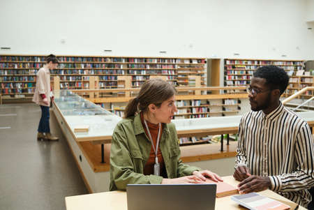 Young people working at the table together and discussing reading of the books in the libraryの写真素材