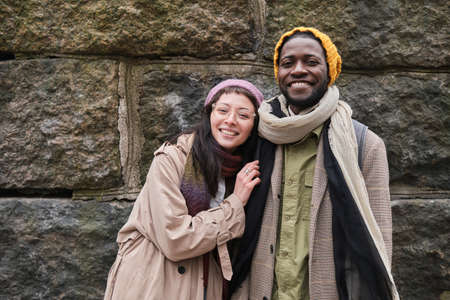 Portrait of happy young couple in warm clothing smiling at camera standing in the city
