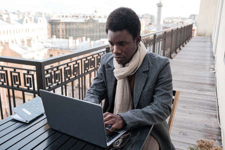 African young businessman working online on laptop while sitting at the table in outdoor cafeの写真素材