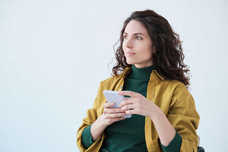 Young pretty woman with curly hair sitting on chair with mobile phone isolated on white background