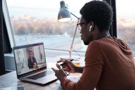 African young businessman talking to his colleague online using laptop while working at office