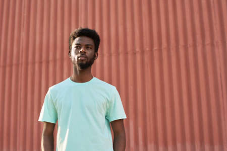 African young man looking away while standing in the city against the red wallの写真素材