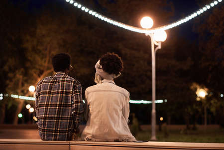 Rear view of young couple sitting on the bench during romantic date in the evening in the parkの写真素材