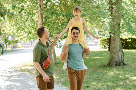 Gay male couple having fun outdoors with their little daughterの写真素材
