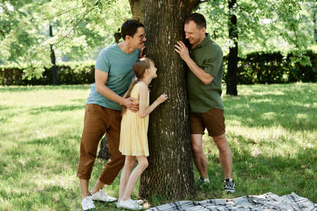 Gay male couple playing with their adopted daughter outdoors in the parkの写真素材