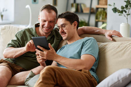 Two friends watching something on digital tablet while sitting on sofa in the roomの写真素材