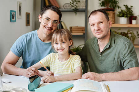 Portrait of gay family with their adopted daughter smiling at camera while studying together at the tableの写真素材