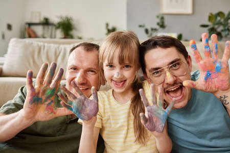 Portrait of happy gay family with child showing their painted hands and smiling at cameraの写真素材
