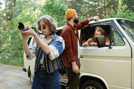 Young woman photographing the nature while travelling by car with her friends