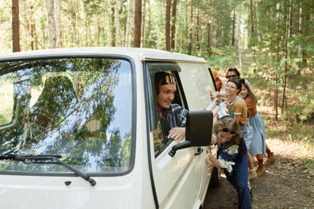 Driver sitting in broken van with people pushing it together in the background in the forest
