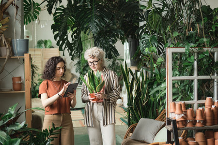 Young woman using digital tablet while examining the new kind of plant together with her colleague in the gardenの写真素材