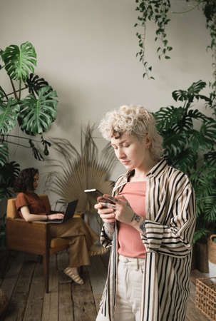 Young businesswoman using her mobile phone and working online with her colleague sitting on armchair...
