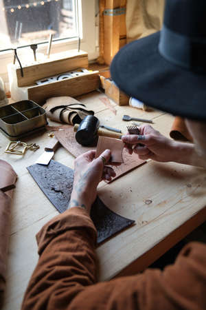 Close-up of carpenter sitting at the table and working with leather, he repairing products