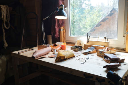 Image of workplace of carpenter with work tools and pieces of leather material on the table in workshopの写真素材