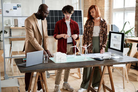 Group of engineers standing at the table and discussing project together during their teamwork at...