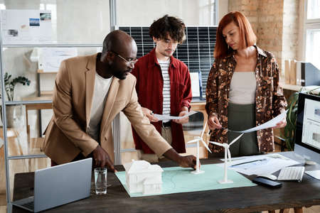 Group of engineers developing new project with models while standing around the table at office