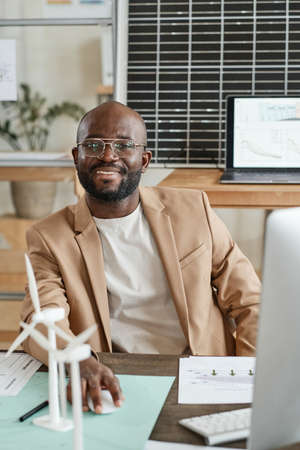 Portrait of African architect smiling at camera while developing new design project with computer at the tableの写真素材
